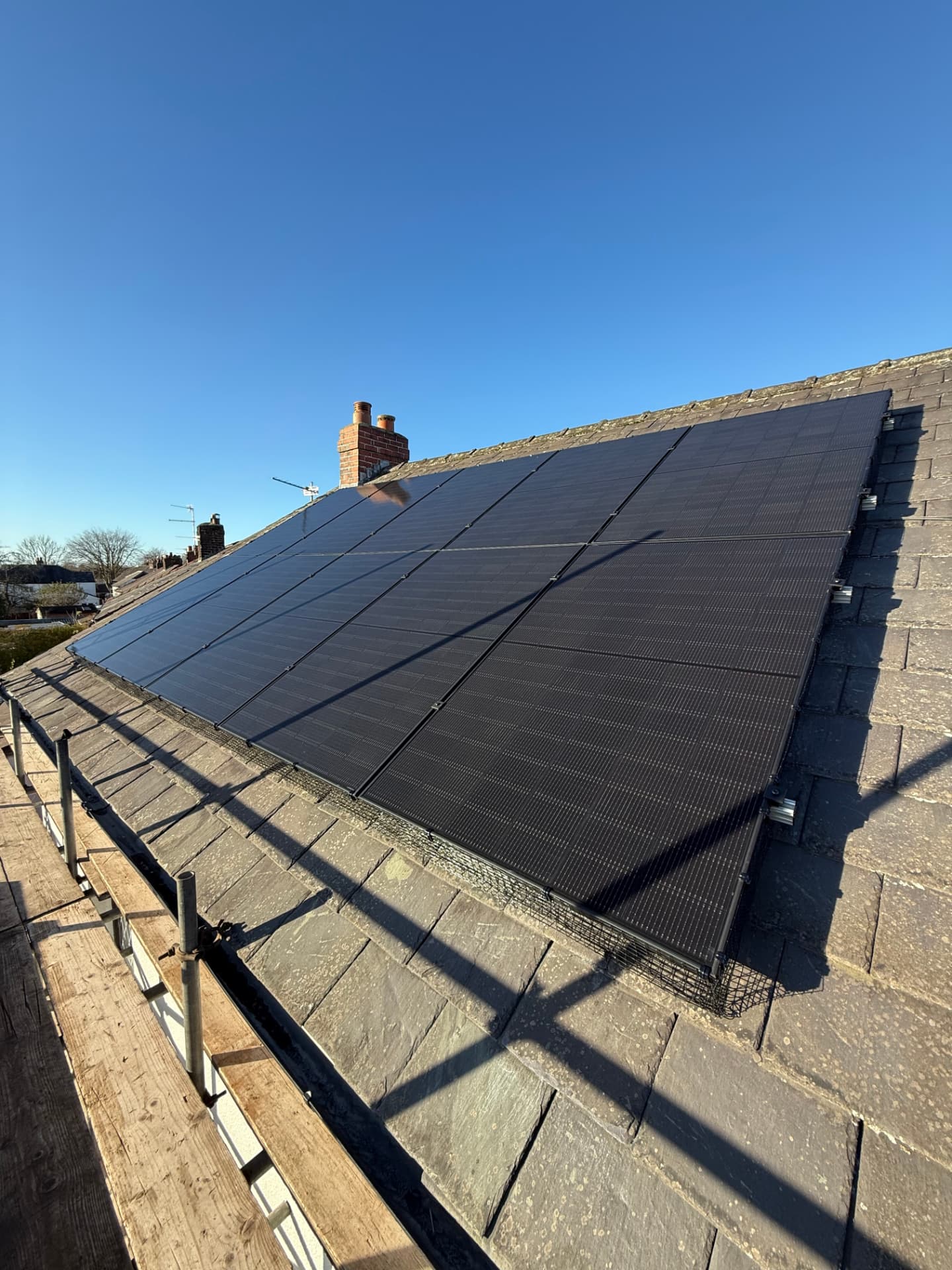 Ten solar panels with bird-proofing mesh on a slated roof in Penwortham, seen from scaffolding